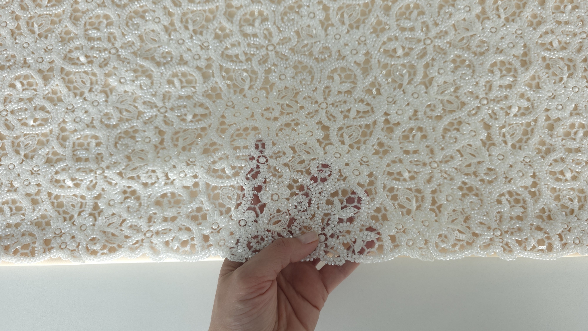 Material cu mărgele și paiete la metru ținut în mână pentru a arăta transparența