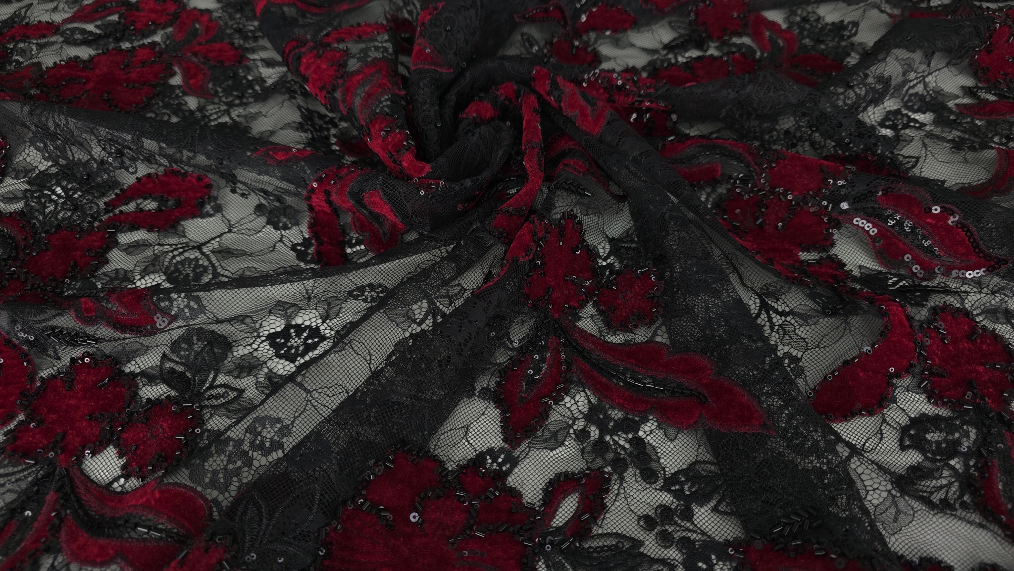 Material strâns în falduri ample, flori roșu sânge și micropaiete vizibile