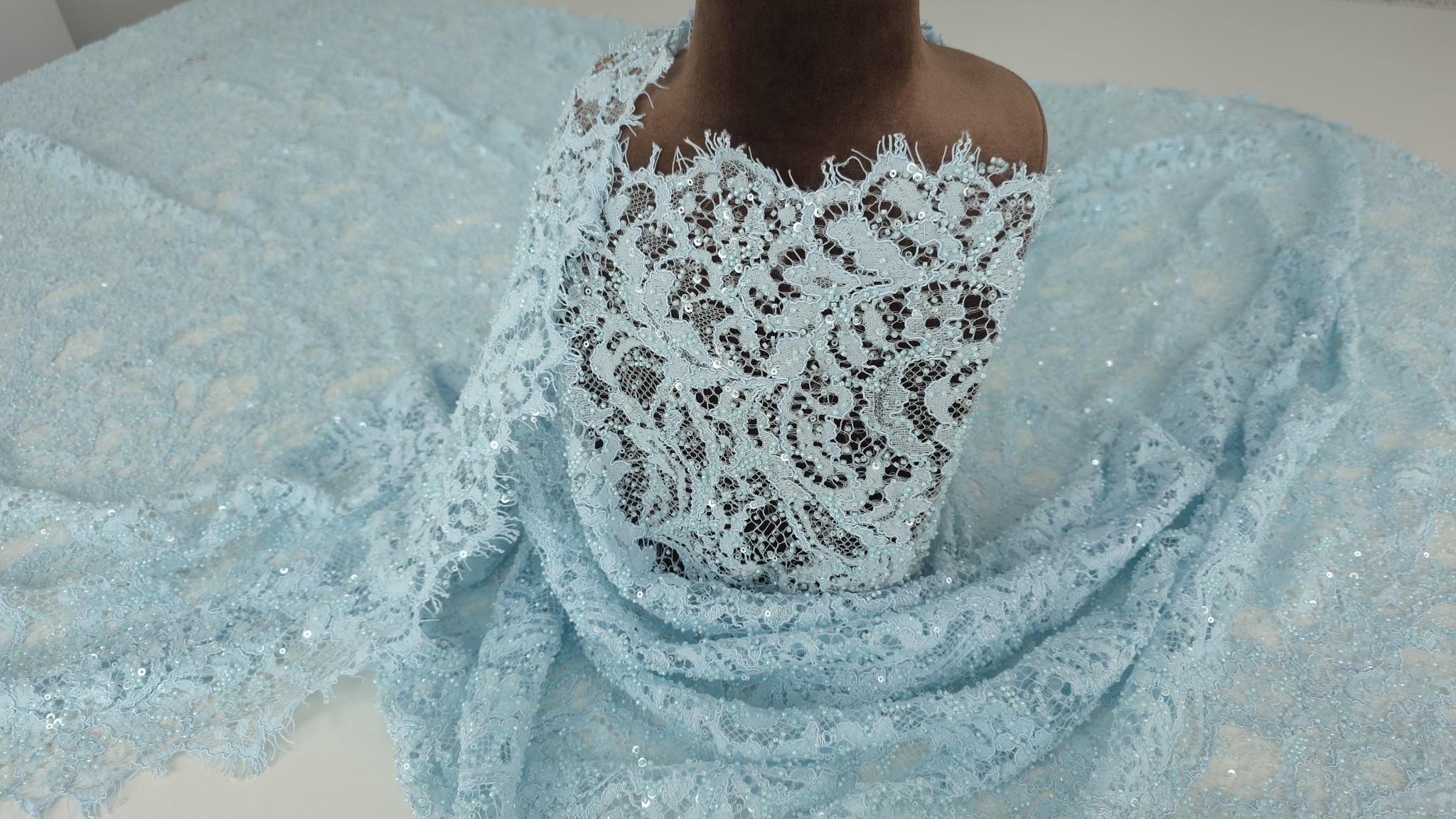 Material textil drapat pe manechin cu falduri ample și bordură scalopată vizibilă pe margini