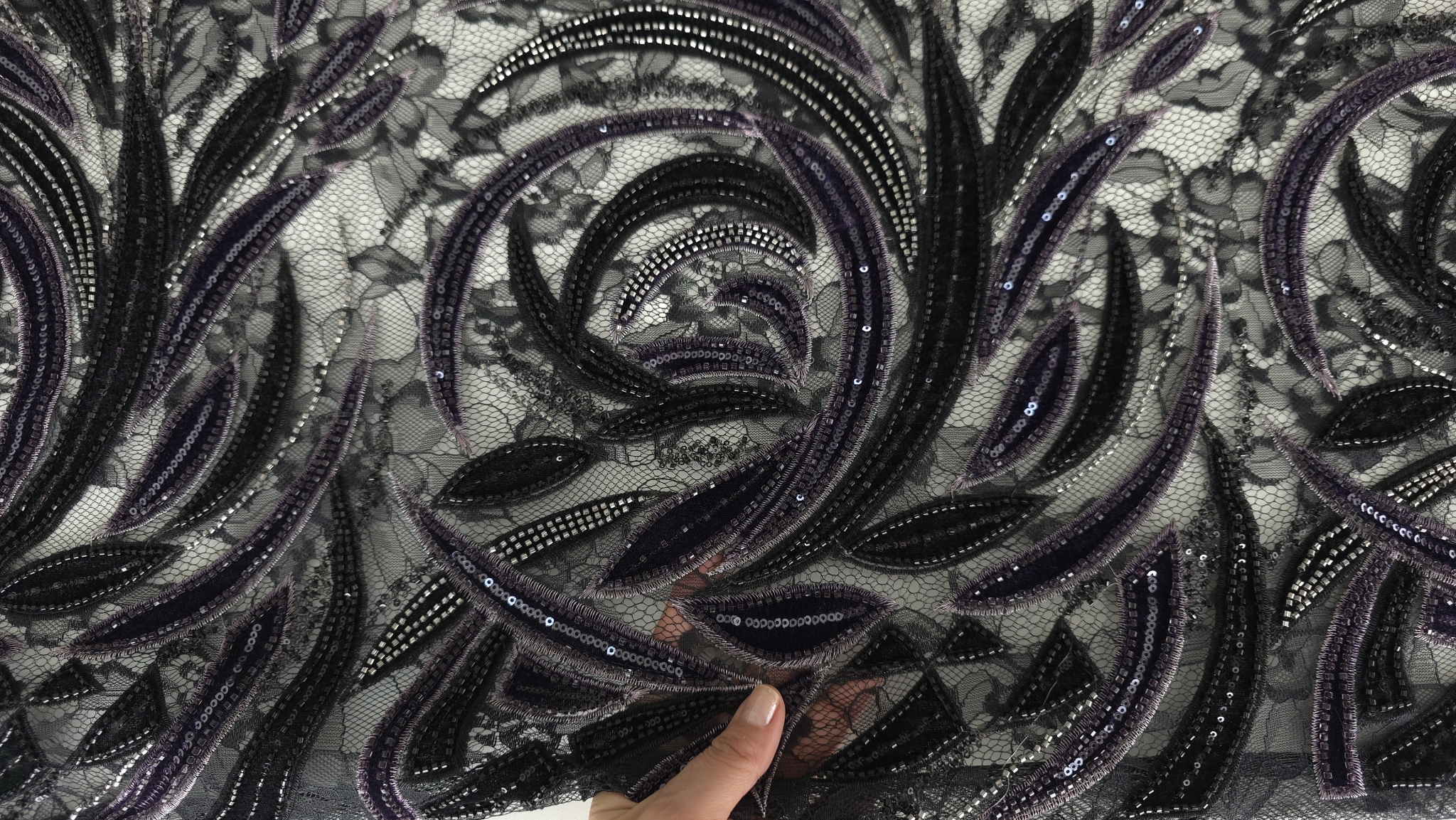 Materialul ținut în mână, tulle transparent cu frunze ondulate și margele argintii vizibile