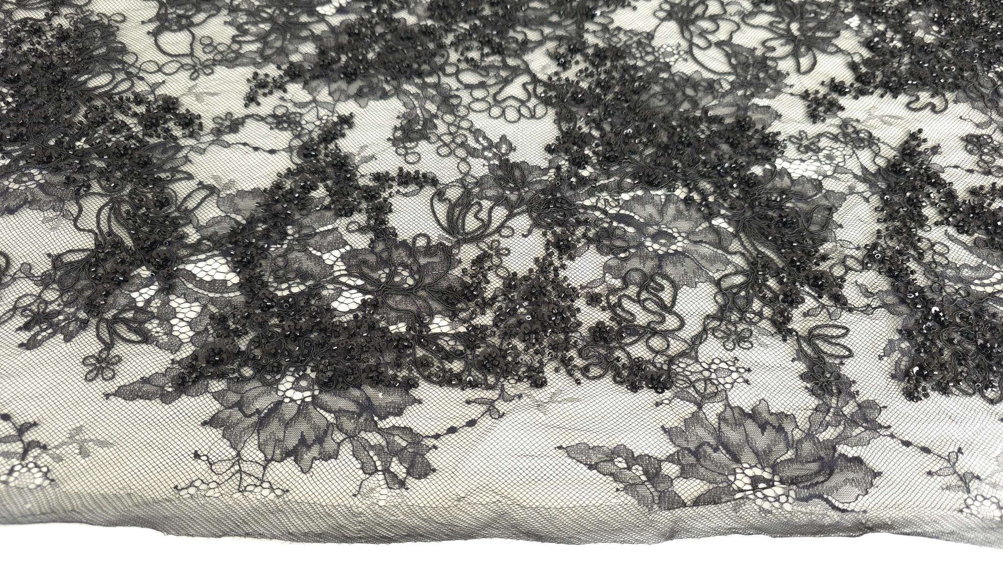 Metraj dantelă neagră cu margele și paiete formând falduri în lumină laterală