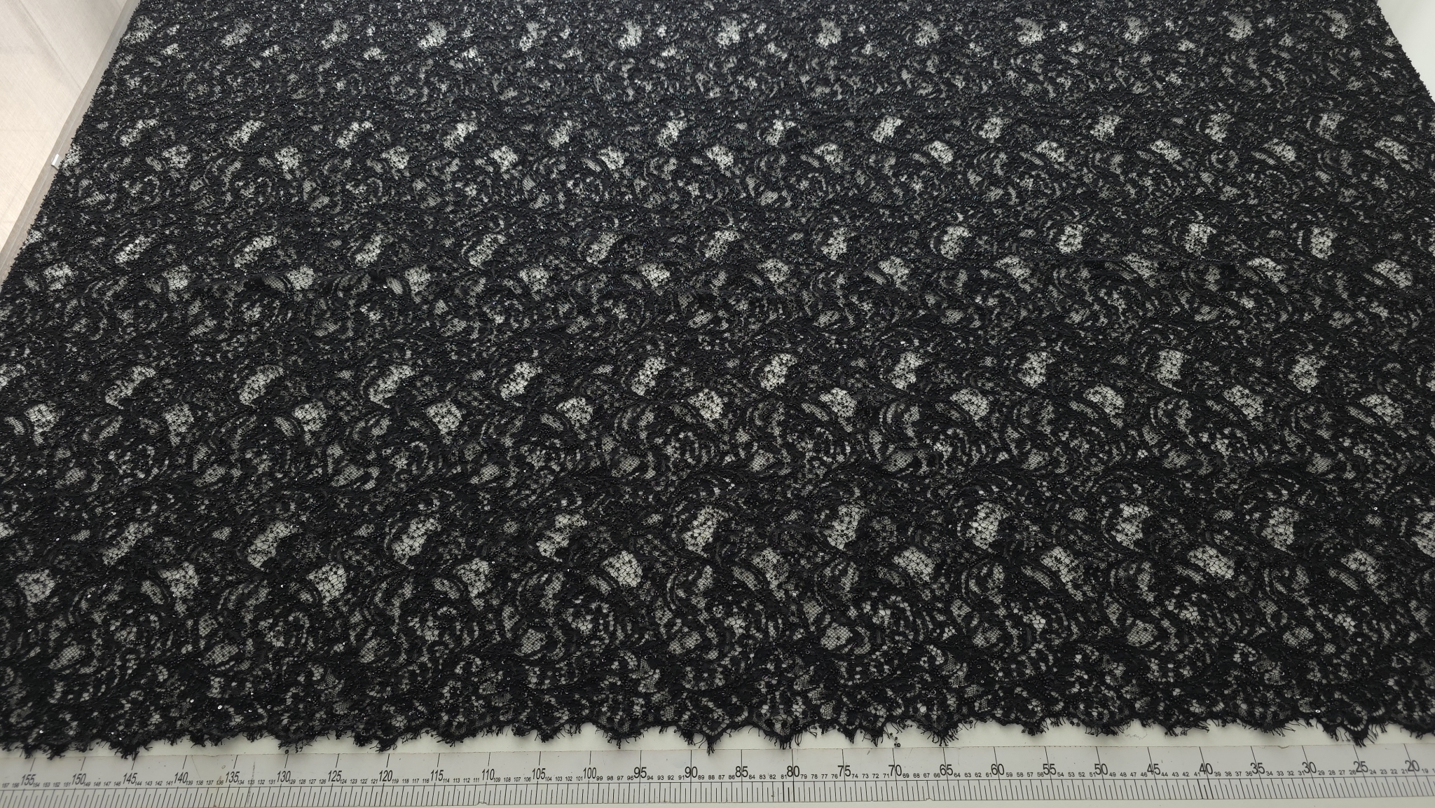 Metraj negru cu paiete la metru desfăcut pe masă de tăiere cu riglă gradată