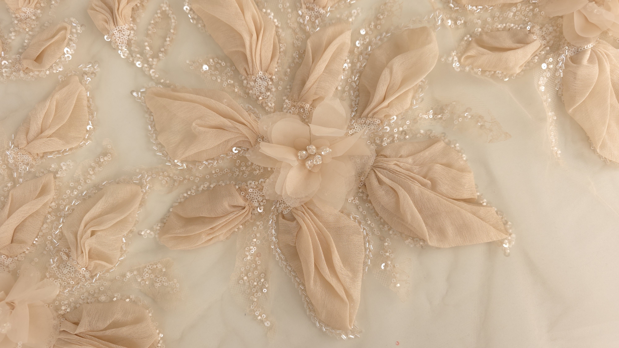 Petale peach supradimensionate și paiete transparente cusute pe ramuri florale, plan apropiat