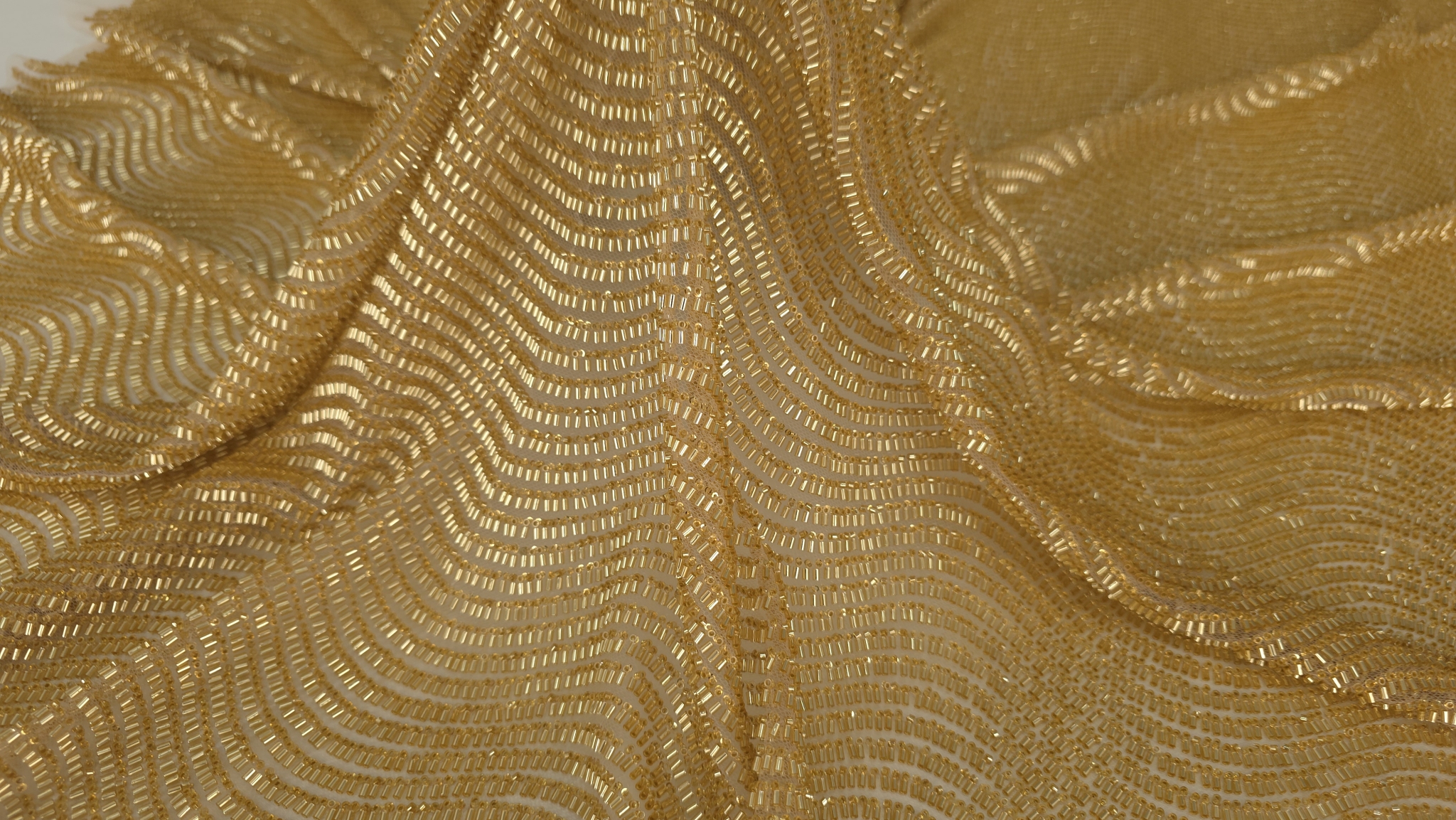 Rânduri ondulate dense de mărgele tubulare aurii cu tul transparent vizibil între linii