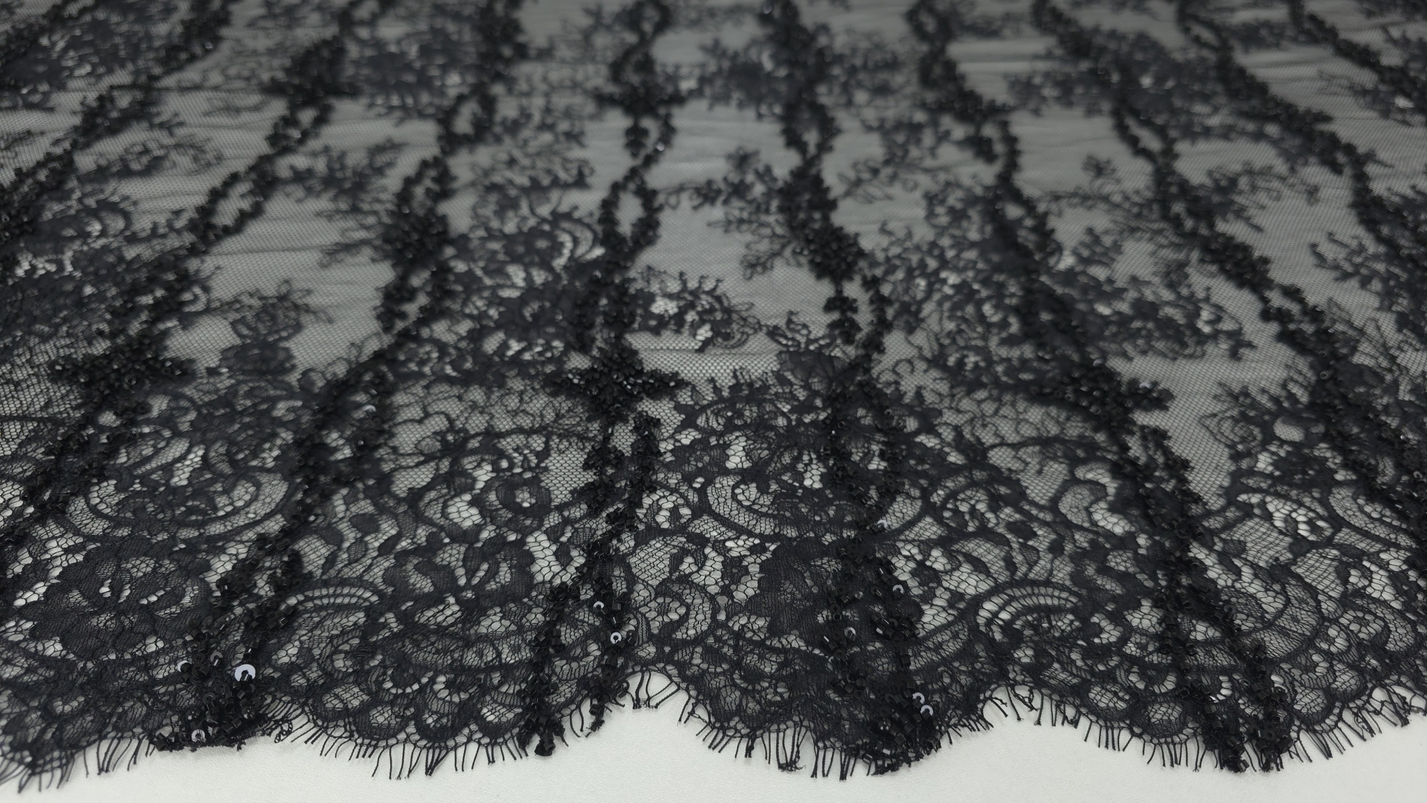 Suprafața dantelei negre cu micropaiete și mărgele văzută din unghi lateral