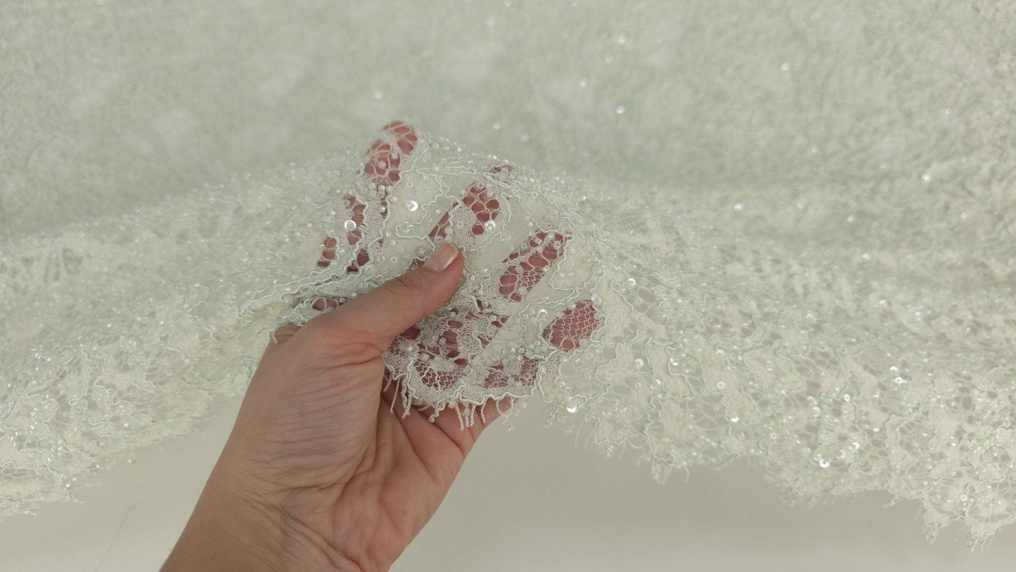 Suprafață textilă verde mint cu paiete și mărgele distribuite pe desen vegetal