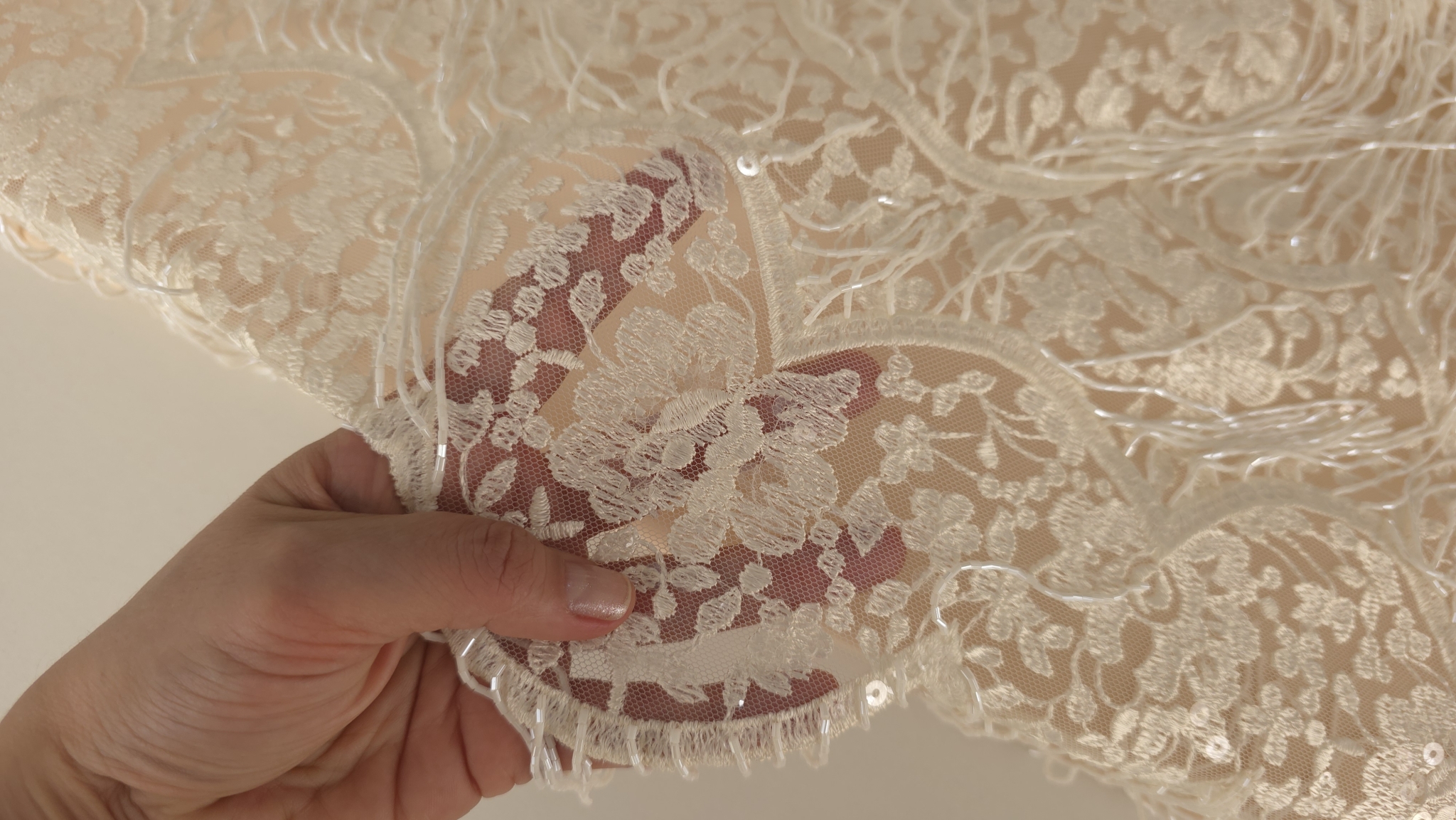 Transparența tullului brodat evidențiată prin suprapunerea pe palmă cu franjuri vizibili