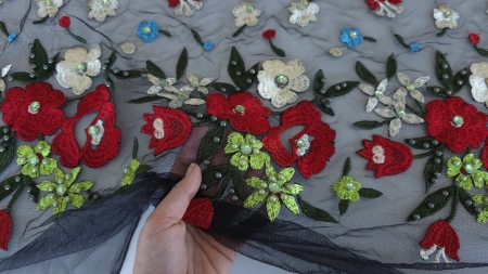 Tulle brodat cu margele si pietre vazut in transparenta, tinut in mana pentru a ilustra finetea materialului si a aplicatiilor lucioase