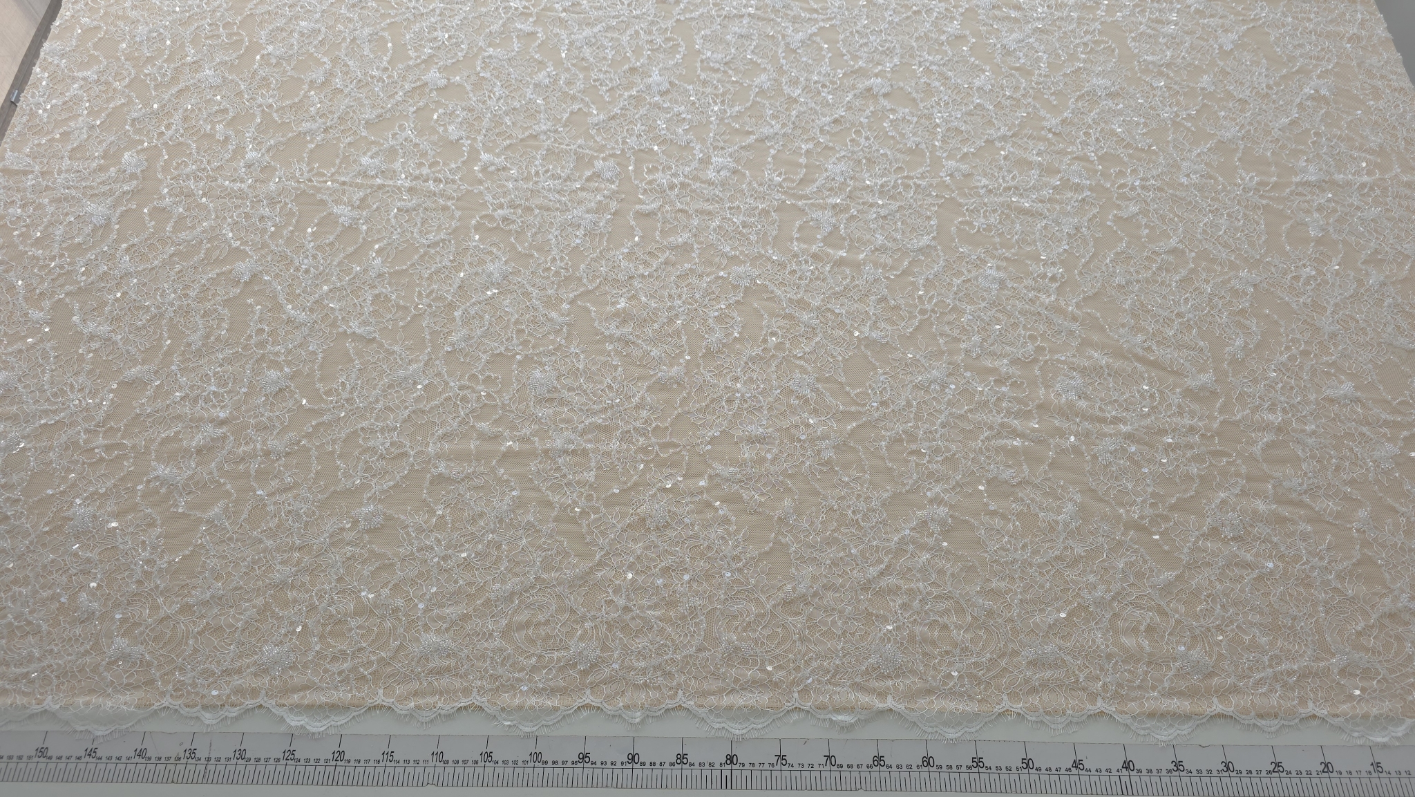 dantela ivory tip chantilly cu margele si paiete elodie materialul desfasurat pe masa cu rigla de masurare