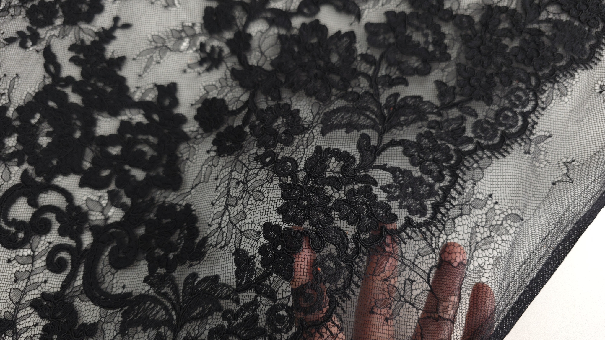 mâna sub dantelă evidențiind opacitatea broderiei în contrast cu plasa invizibilă