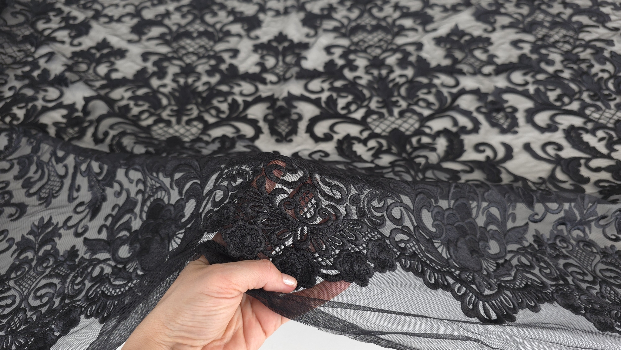 Mână ridicând marginea festonată, pielea vizibilă prin stratul transparent