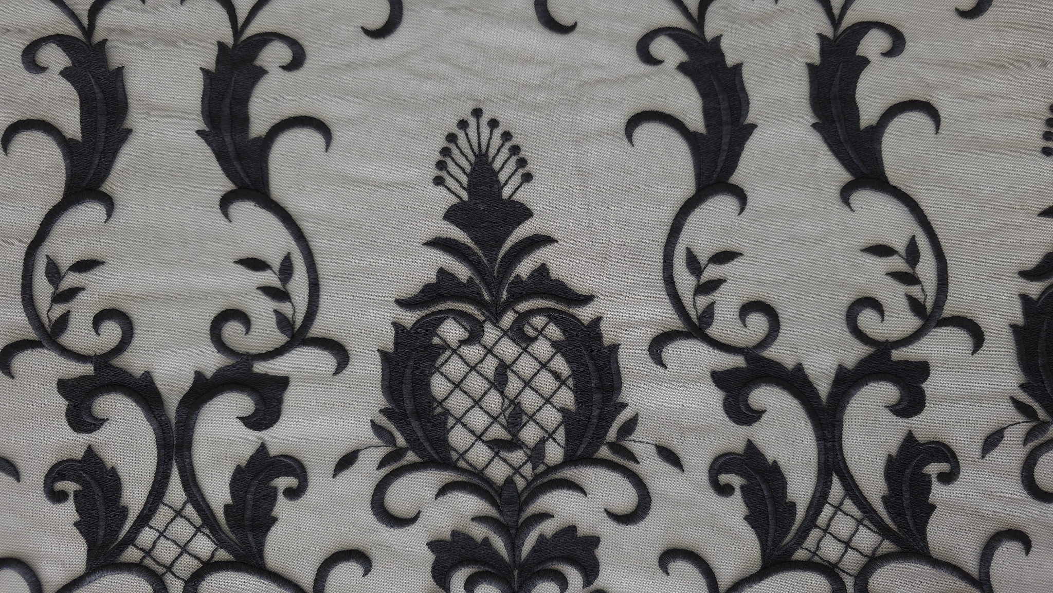 Detaliu margine ondulată cu volute și frunze pe material în nuanță închisă