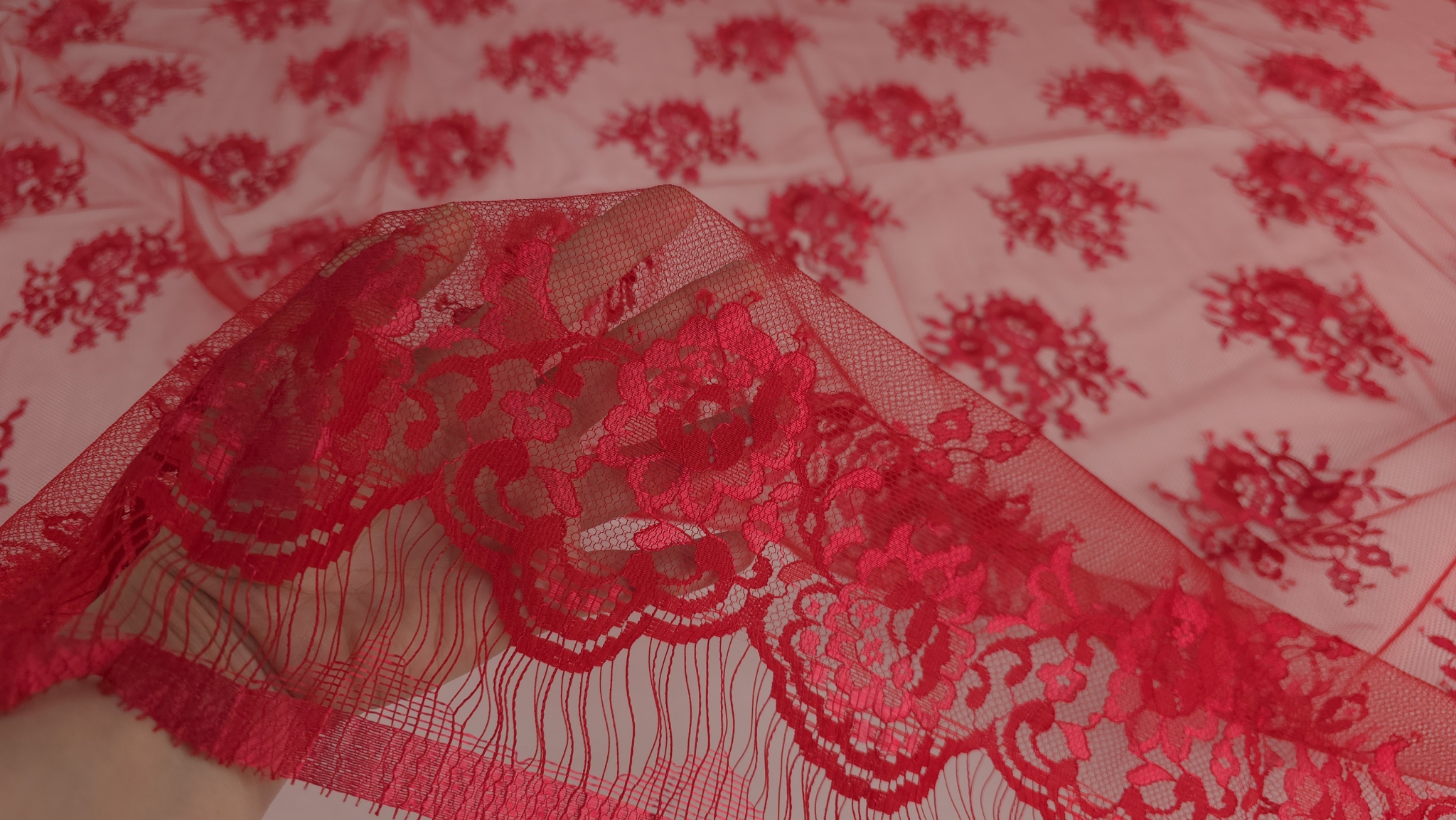 Bordura ondulată cu franjuri a dantelei Chantilly roșu Ferrari ridicată între degete