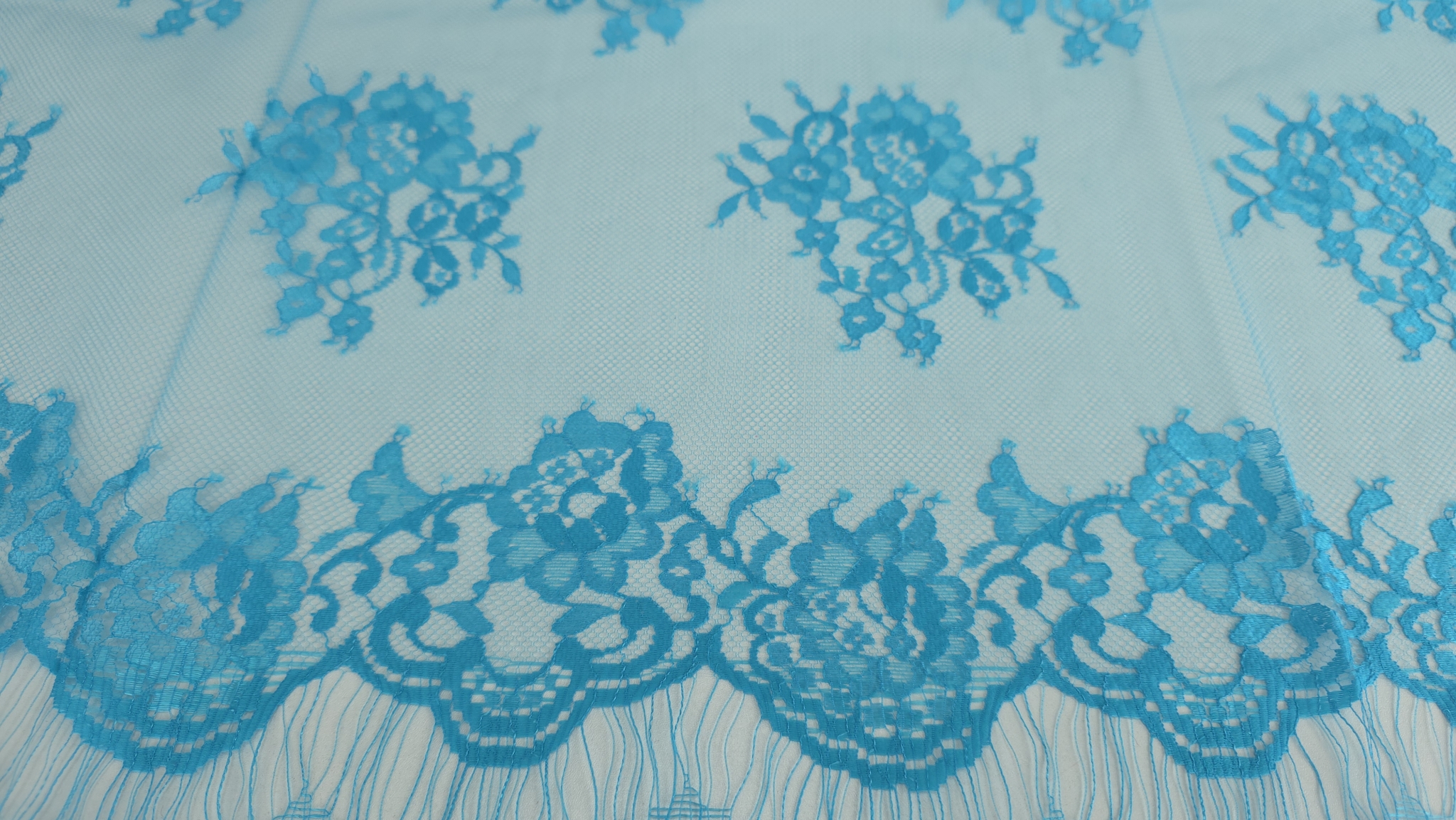 Bordura ondulată cu franjuri și motive florale dense turquoise pe marginea dantelei Chantilly