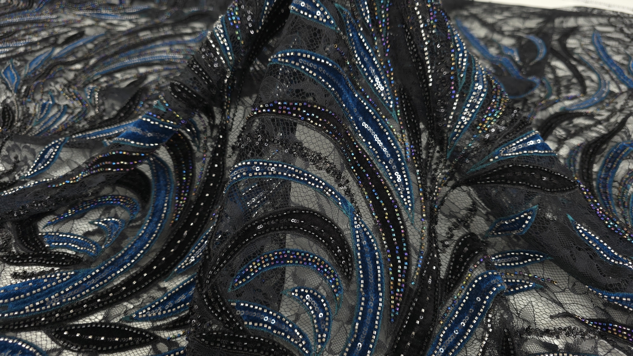 Caderea naturală a materialului în falduri cu spirale turcoaz și negre din catifea, margele vizibile