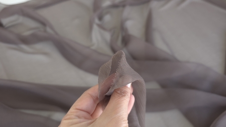 Voal creponat mocha mousse muselină din mătase naturală ținut între degete cu textură creponată vizibilă