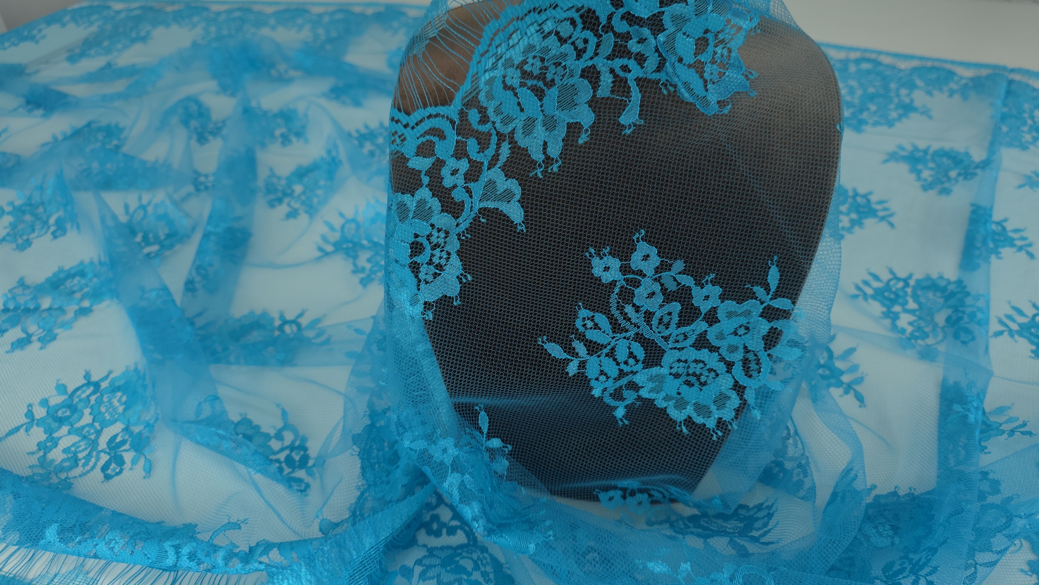 Dantela Chantilly turquoise aruncată pe manechin cu bordura ondulată și buchete florale în plan secund