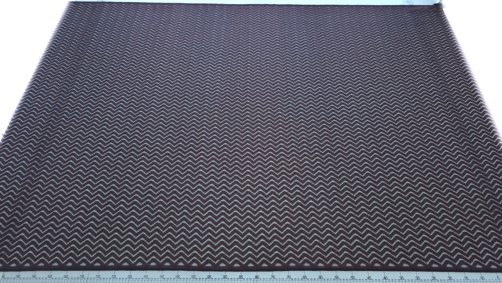 Dantelă neagră cu fir metalizat roșu model zigzag întinsă pe masă cu riglă de măsurare