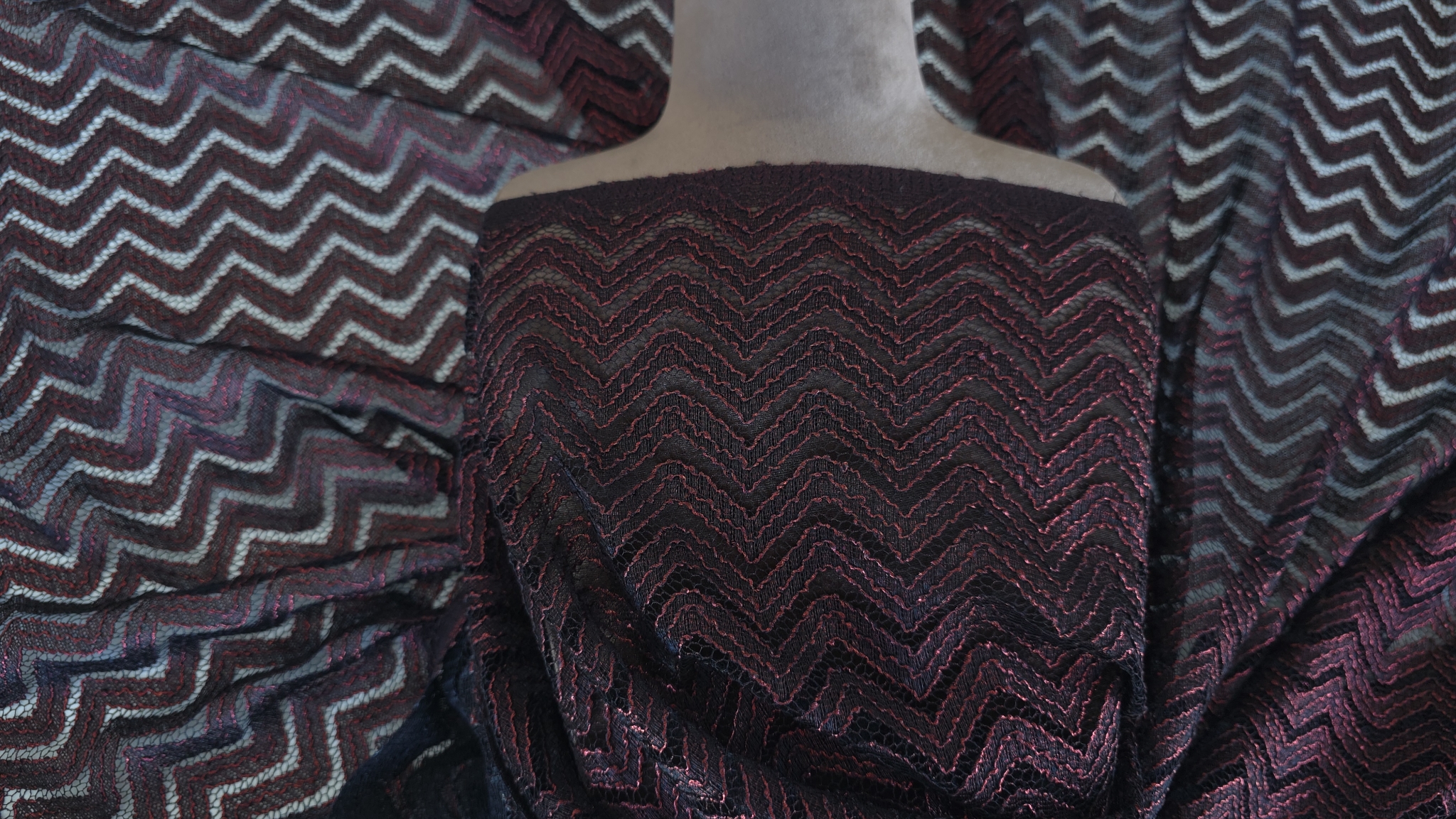 Dantelă neagră cu fir metalizat roșu model zigzag prezentată pe bust de manechin