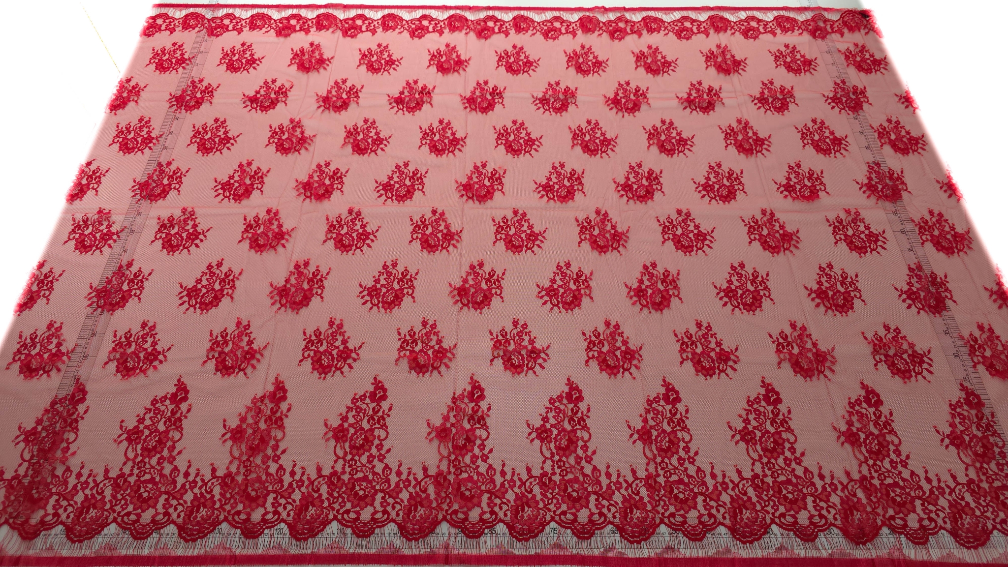 Dantela tip Chantilly rosu Ferrari întinsă pe suprafață cu rigla laterală și motive florale uniforme
