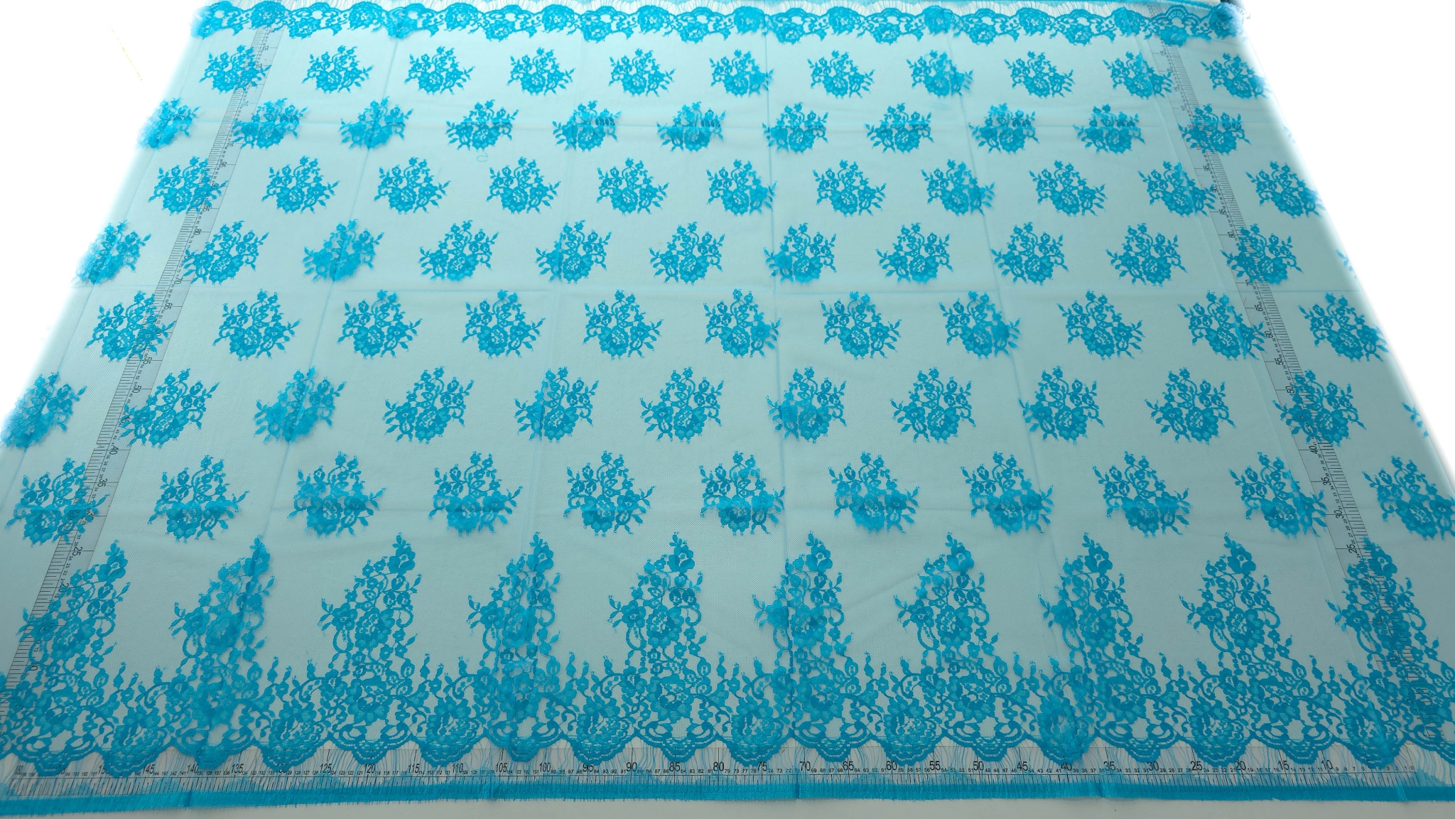 Dantela tip Chantilly turquoise desfășurată integral cu rigle laterale și bordura ondulată la bază