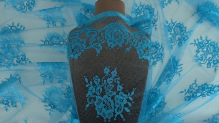 Dantela tip Chantilly turquoise drapată pe manechin maro cu bordura și buchete florale vizibile