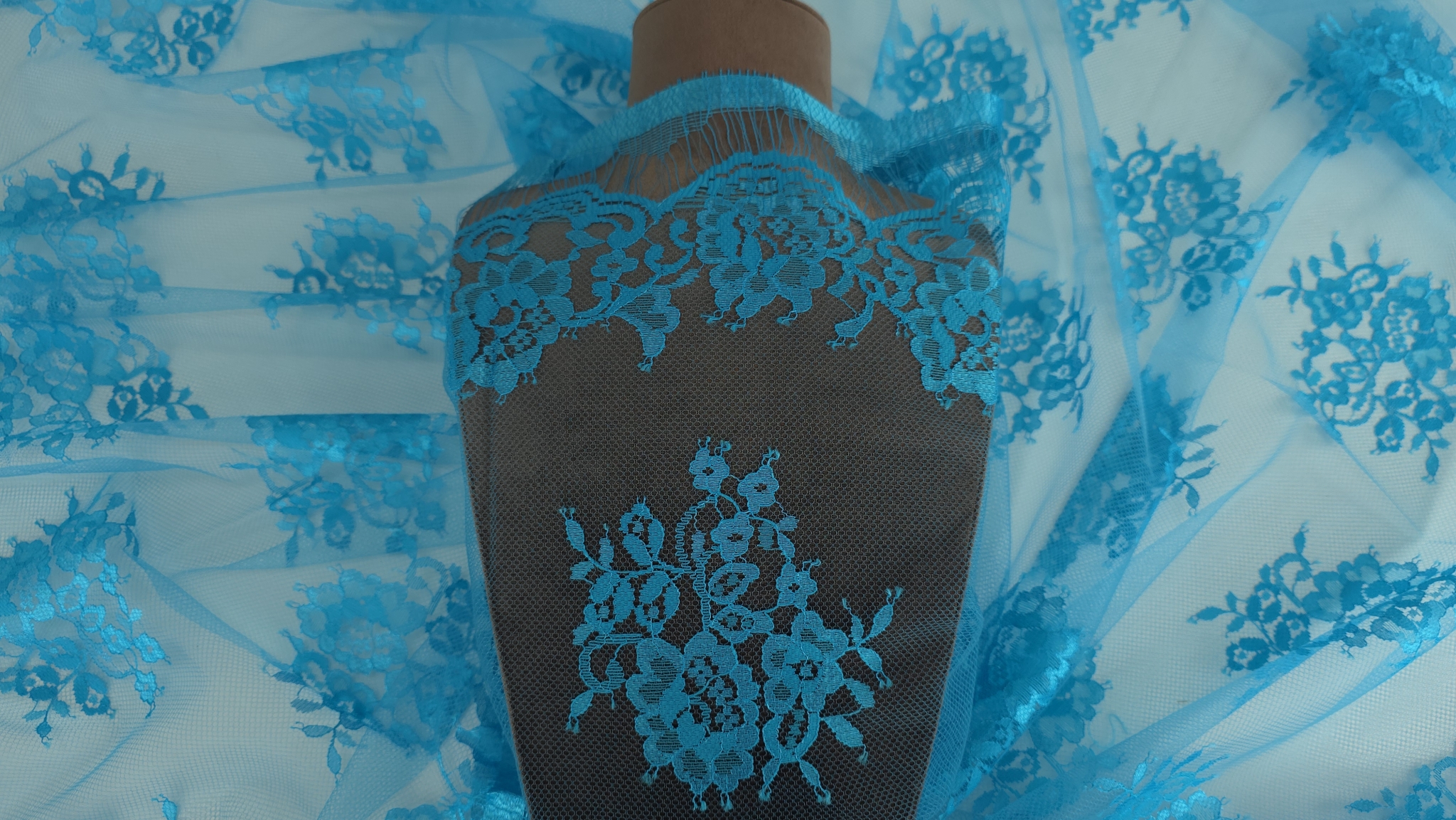 Dantela tip Chantilly turquoise drapată pe manechin maro cu bordura și buchete florale vizibile