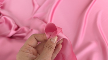Degete care prind colțul unui material satinat roz arătând flexibilitatea