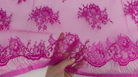 Degetele ridică bordura fuxia cu franjuri pe fond de tull transparent cu buchete florale distribuite deasupra