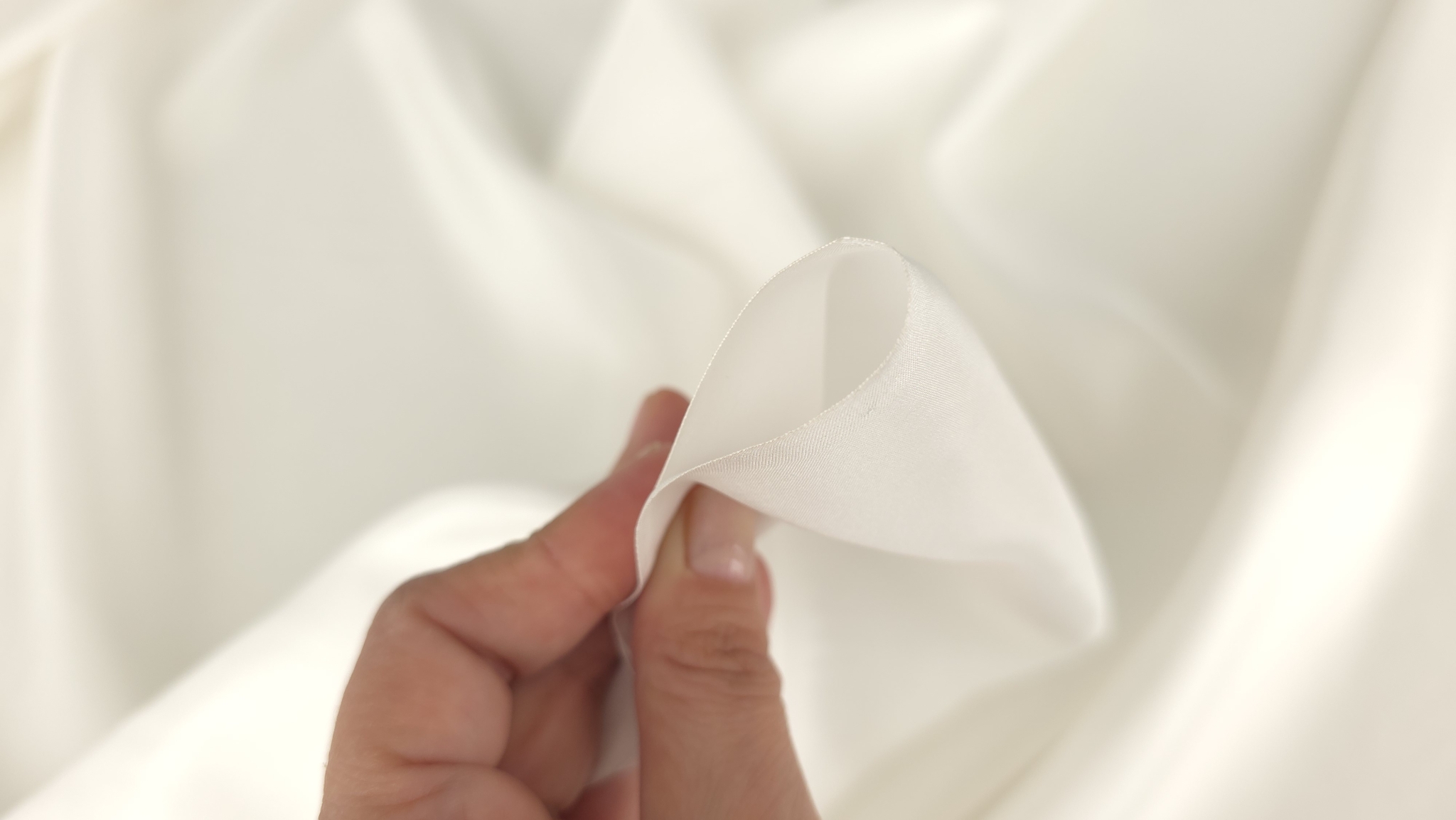 Detaliu cu degetele strângând ușor materialul ivory pentru a evidenția textura fină
