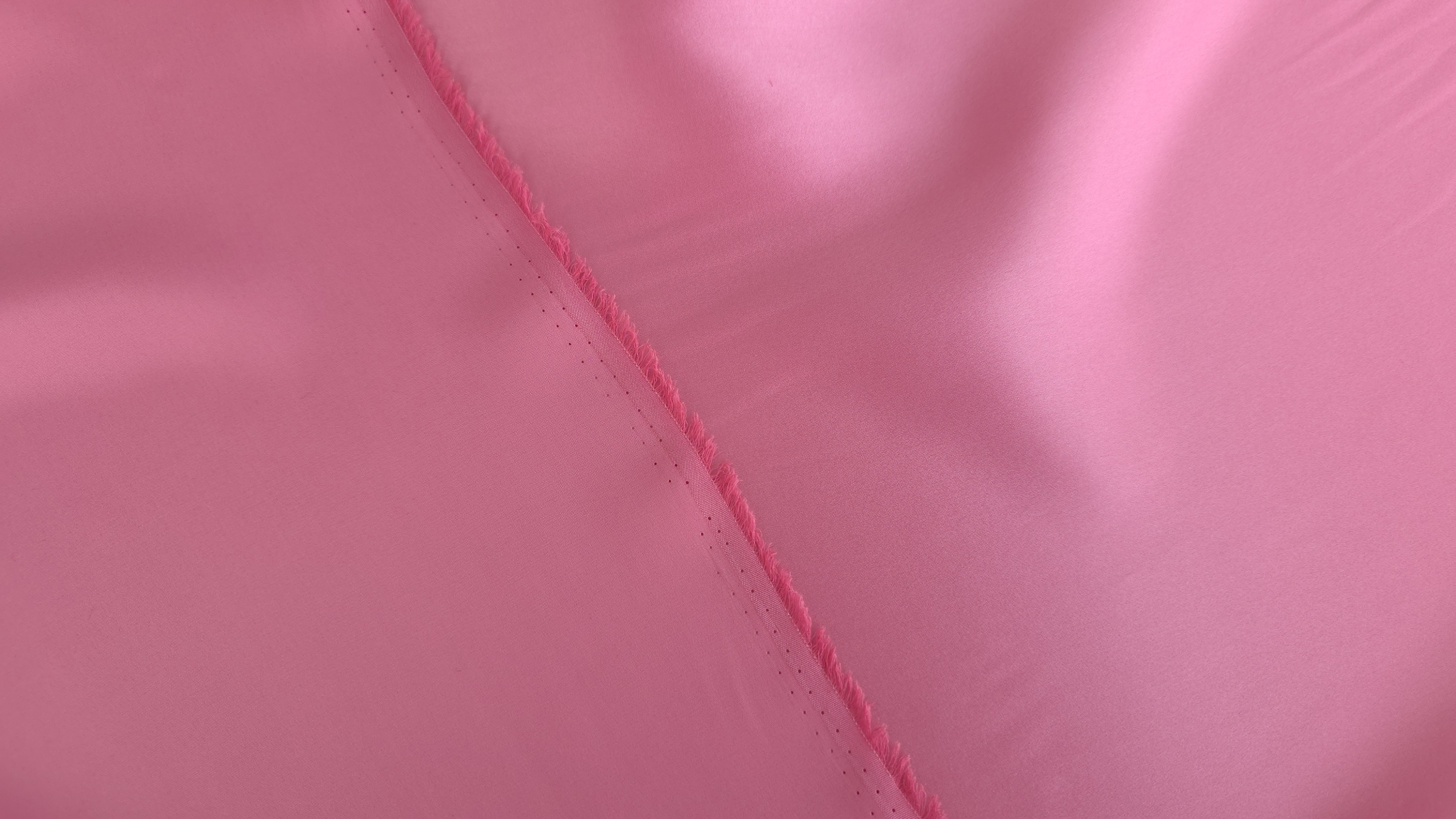 Detaliu de margine cusută pe material satinat roz deschis