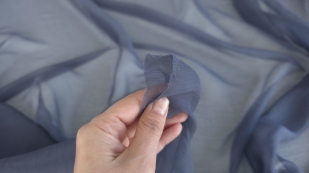 Detaliu de textură creponată a voalului gri metalic ținut în mână