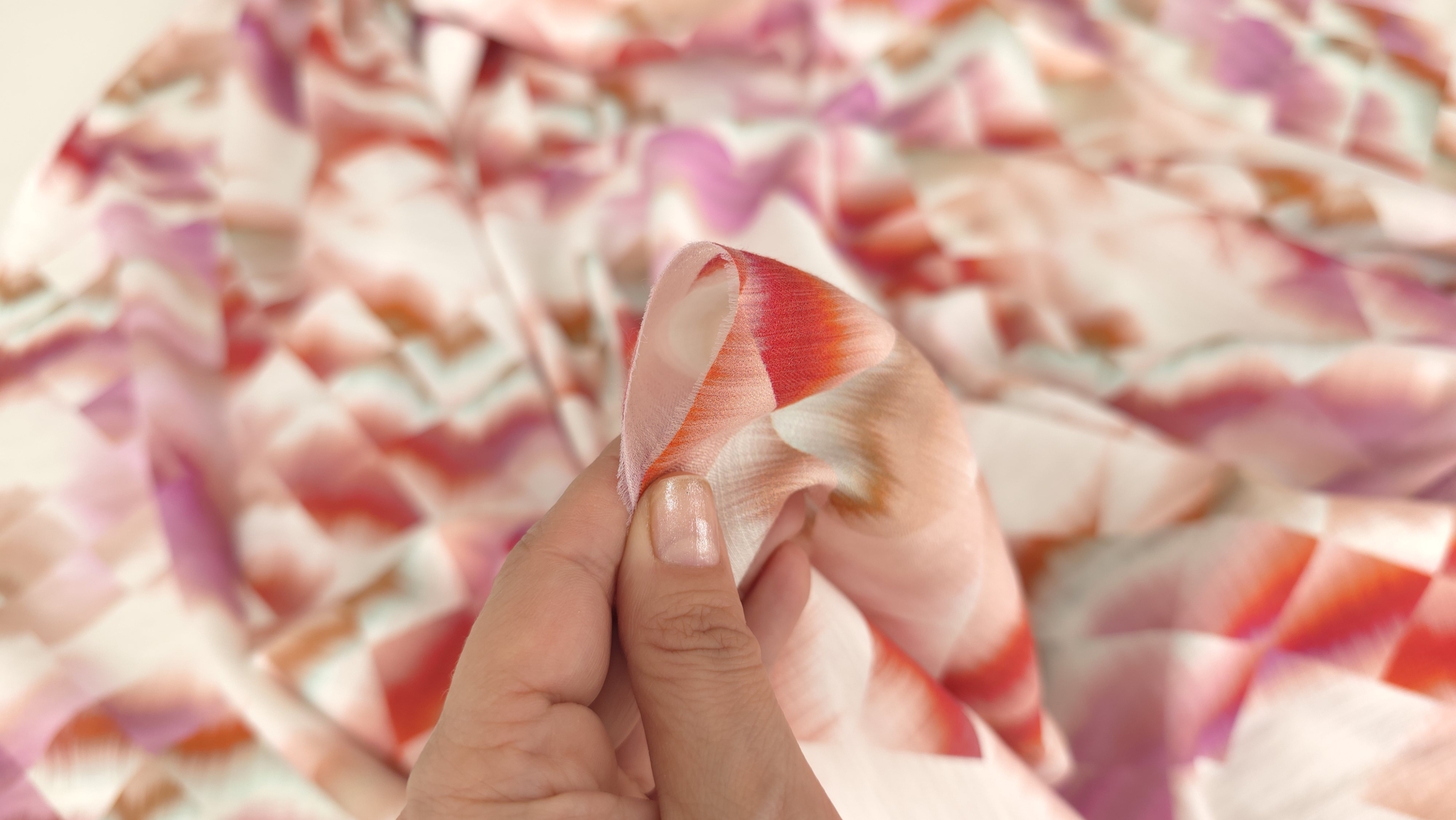 Detaliu între degete al țesăturii vascoza cu print geometric în nuanțe de roz și roșu