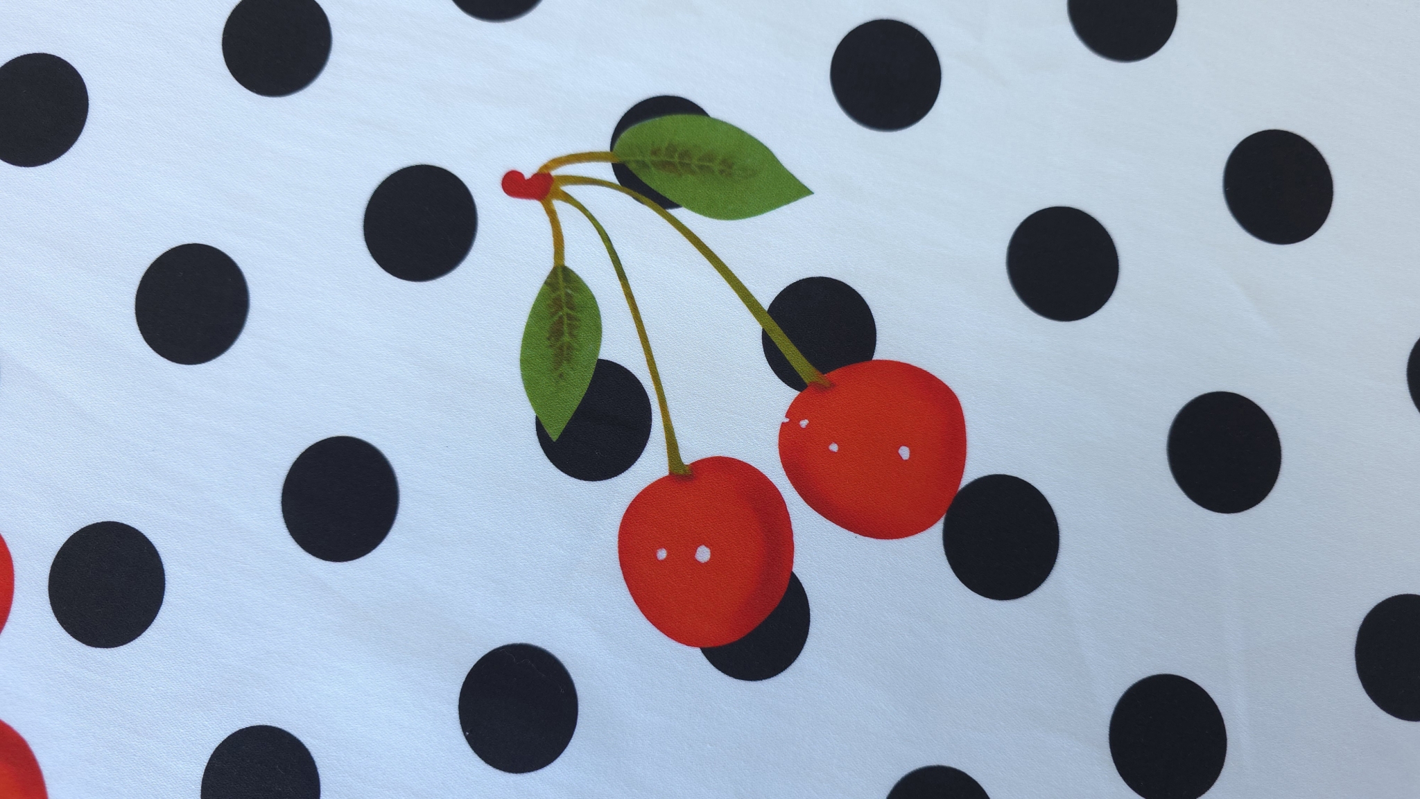 Detaliu plan apropiat al unei perechi de cireșe roșii cu frunze verzi pe denim alb cu buline negre