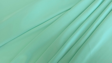 Detaliu textură netedă pe material verde turcoaz pastel, falduri line în plan apropiat