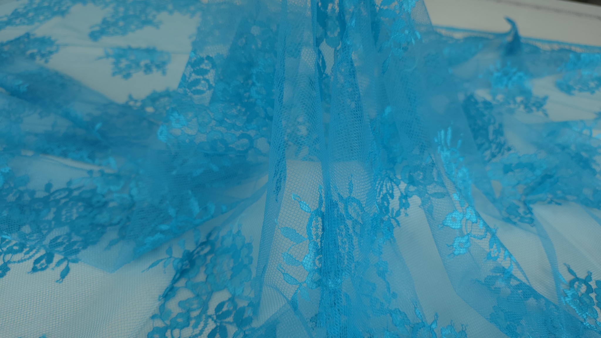Falduri lejere din dantela Chantilly turquoise ridicate de pe suprafață cu tull transparent vizibil