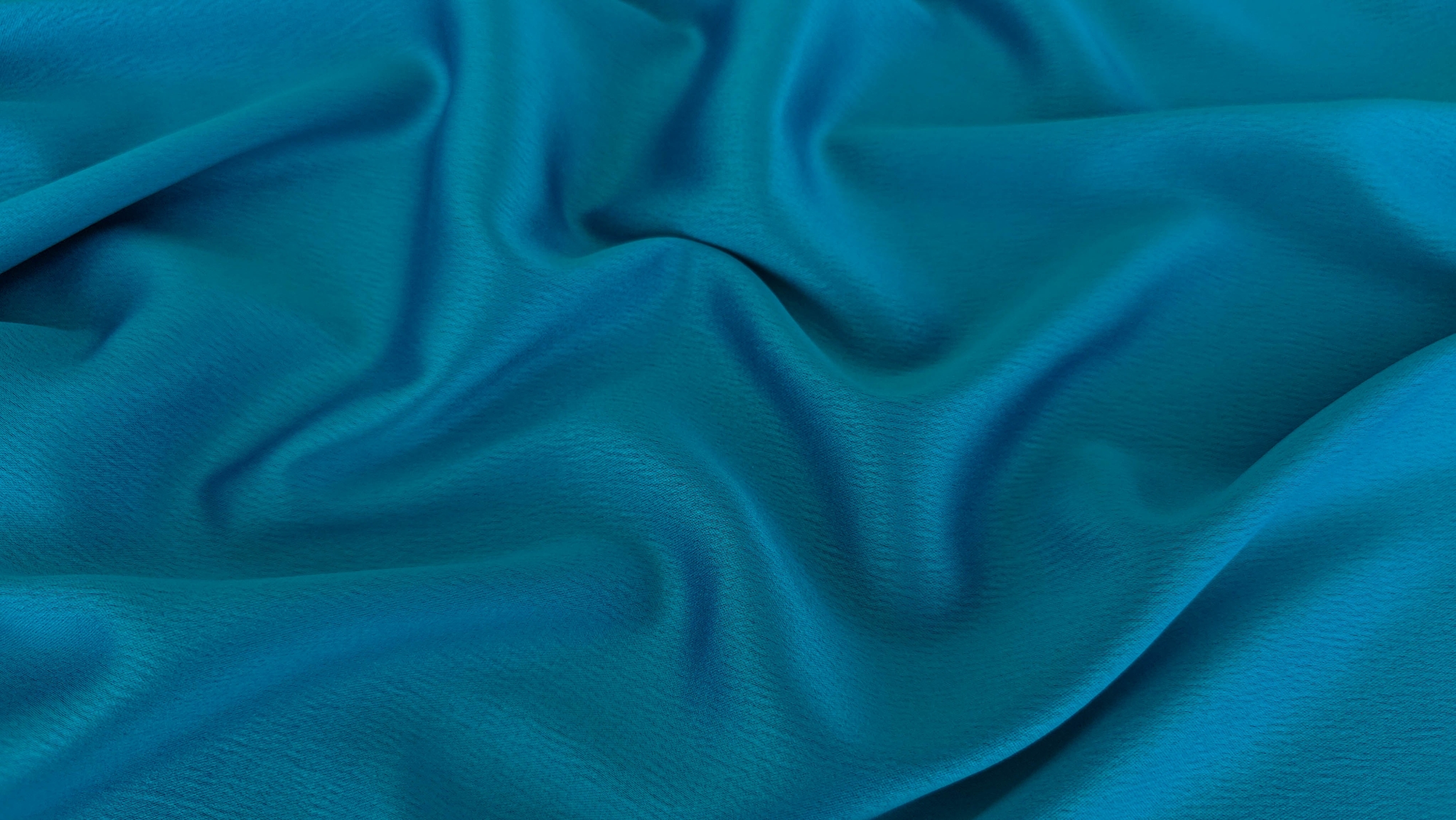 Falduri moi ondulate din tafta albastru turquoise, culoare saturată și uniformă pe toată suprafața