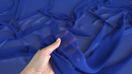 Georgette albastru royal pentru rochii ținut în mână, cu transparență vizibilă în lumină