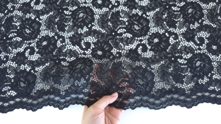 Mână care prezintă marginea festonată a dantelei negre cu motive florale în plan apropiat