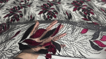 Mână care prezintă transparența tullului negru brodat cu frunze din catifea bordo și negru