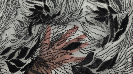 Mână care prezintă transparența tullului negru cu motive florale din catifea