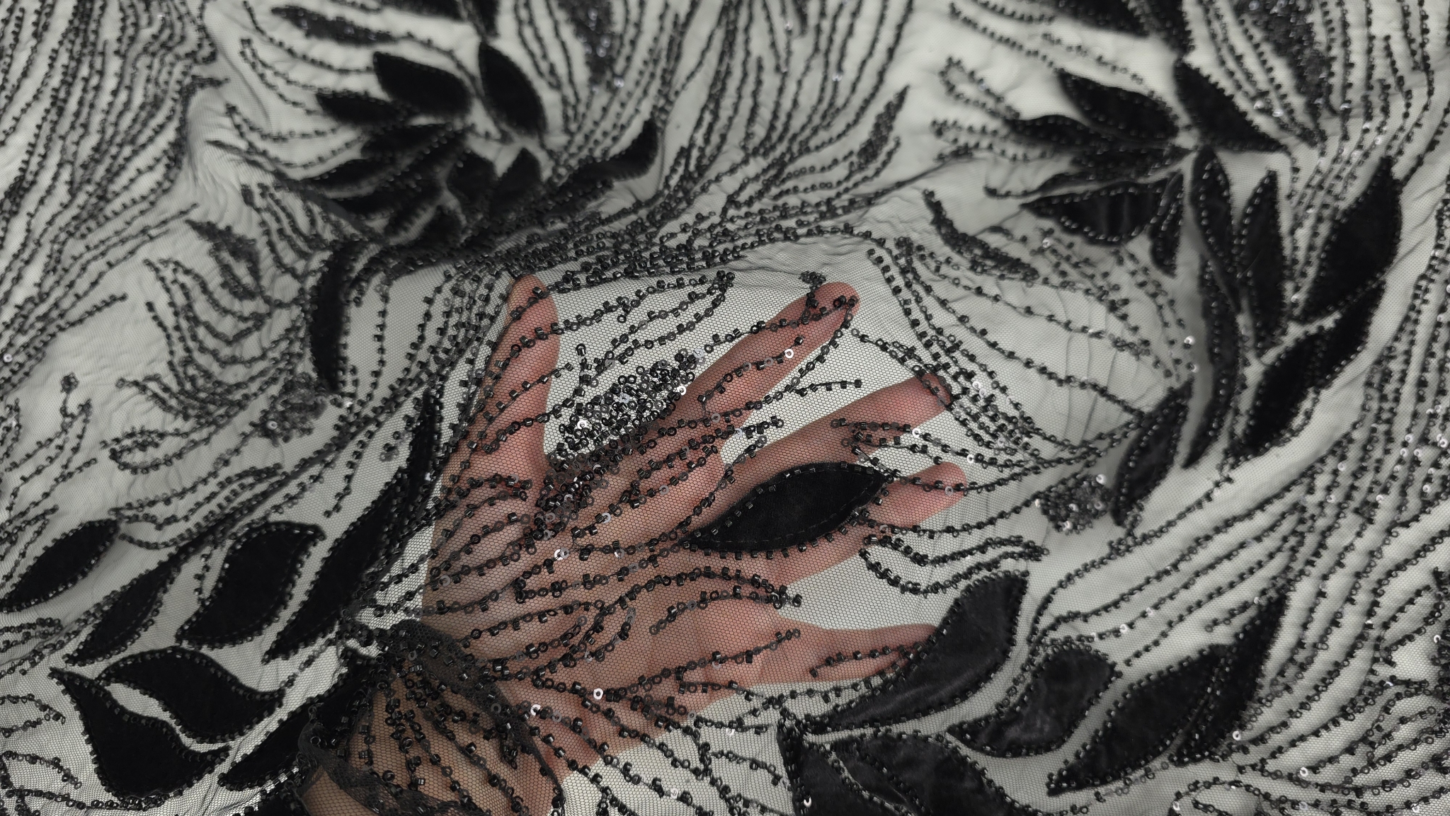 Mână care prezintă transparența tullului negru cu motive florale din catifea