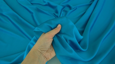 Mână care prinde tafta turquoise strâns, falduri moi grupate cu revenire controlată