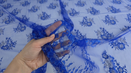 Mână care ridică bordura ondulată cu franjuri fine și buchete florale pe fond translucid