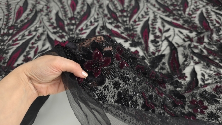 Mână care ridică bordura densă a broderiei cu micropaiete și catifea burgundy
