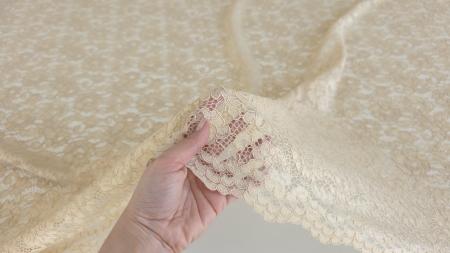 Mână care ridică materialul arătând transparența și bordura festonată