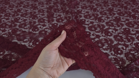 Mână care ridică materialul burgundy arătând bordura festonată și textura florală