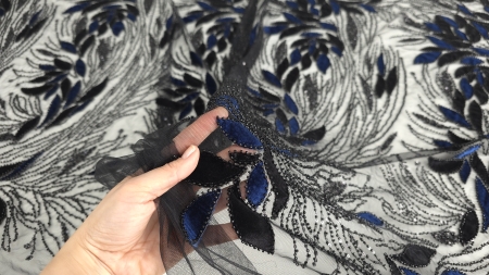 Mână care ridică tullul negru transparent cu frunze bleumarin și negre din catifea conturate cu margele