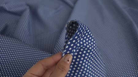 Mână care ridică un colț al materialului cu marginea tăiată destrămată și firele albastre vizibile