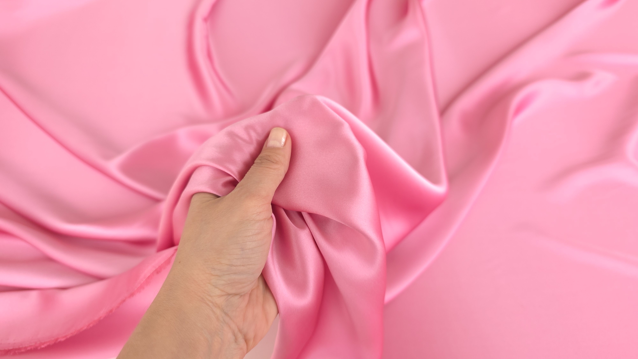 Mână care ține material satinat roz arătând luciul și densitatea țesăturii